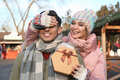 Young woman presenting Christmas gift to her boyfriend at winter fair