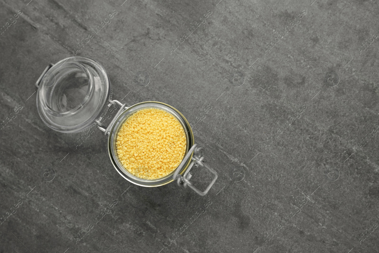 Photo of Glass jar of raw couscous on grey table, top view. Space for text