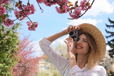 Photo of Happy female tourist taking photo of blossoming sakura outdoors on spring day