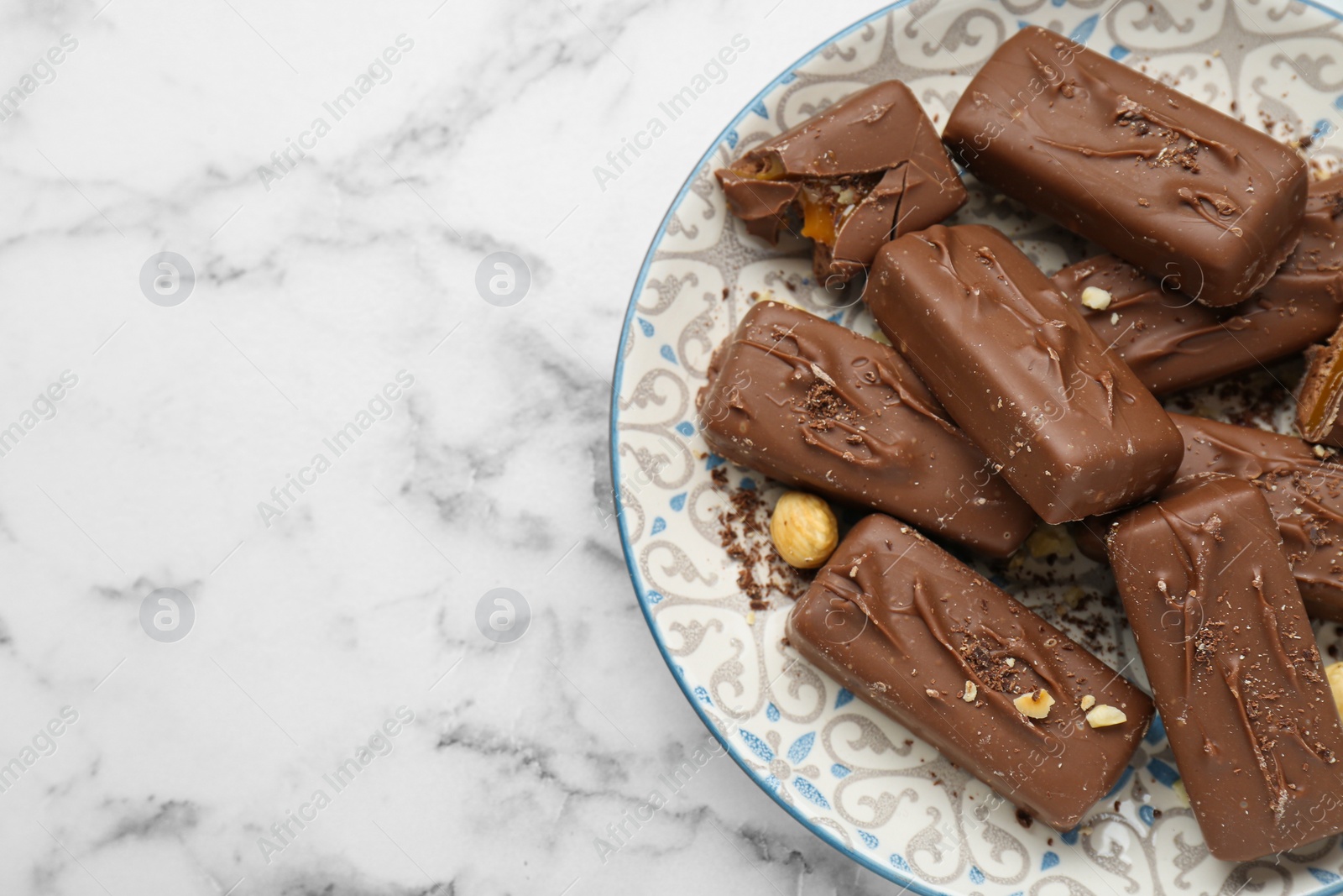 Photo of Delicious chocolate candy bars with nuts on white marble table, top view. Space for text