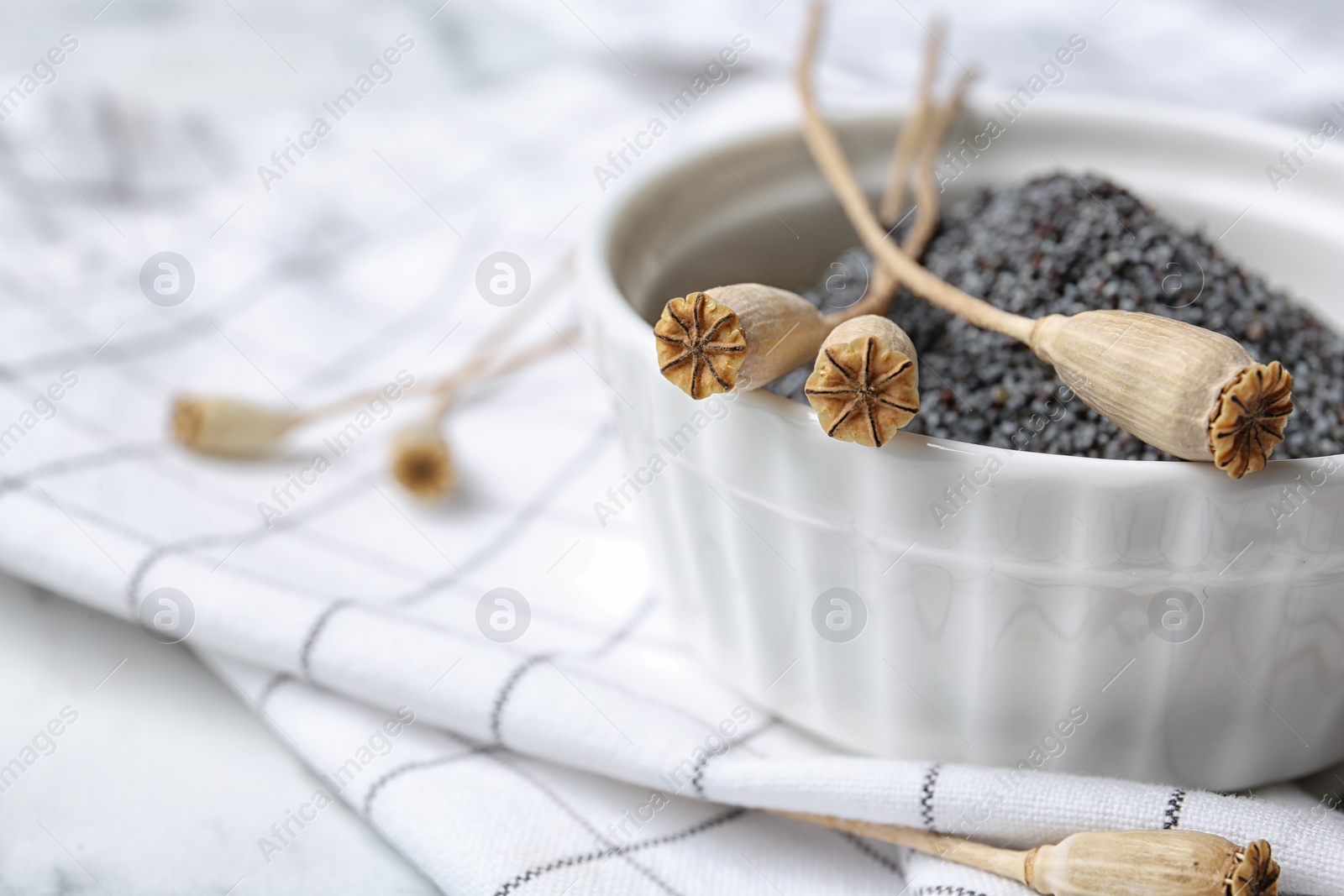 Photo of Bowl with dry poppy heads and seeds on table, closeup