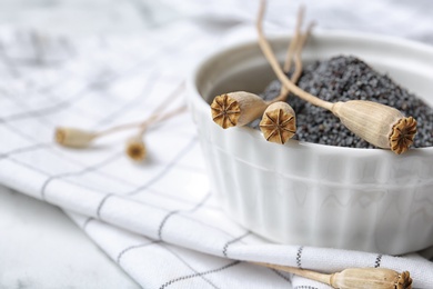 Bowl with dry poppy heads and seeds on table, closeup