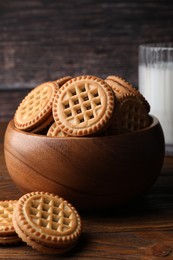 Photo of Tasty sandwich cookies with cream and glass of milk on wooden table