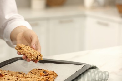 Photo of Woman taking granola bar from baking tray at table in kitchen, closeup. Space for text