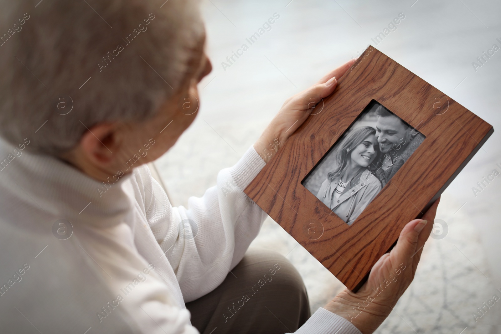 Photo of Elderly woman with framed family portrait at home