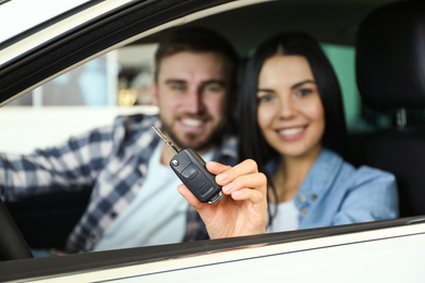 Photo of Happy couple sitting in car at dealership, focus on hand with key