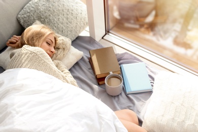 Beautiful young woman sleeping near window at home, above view. Winter atmosphere