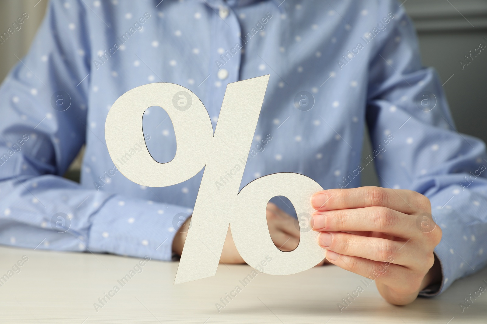 Photo of Woman holding percent sign at white wooden table, closeup