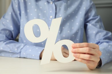 Photo of Woman holding percent sign at white wooden table, closeup