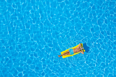 Young man with inflatable mattress in swimming pool, top view. Space for text