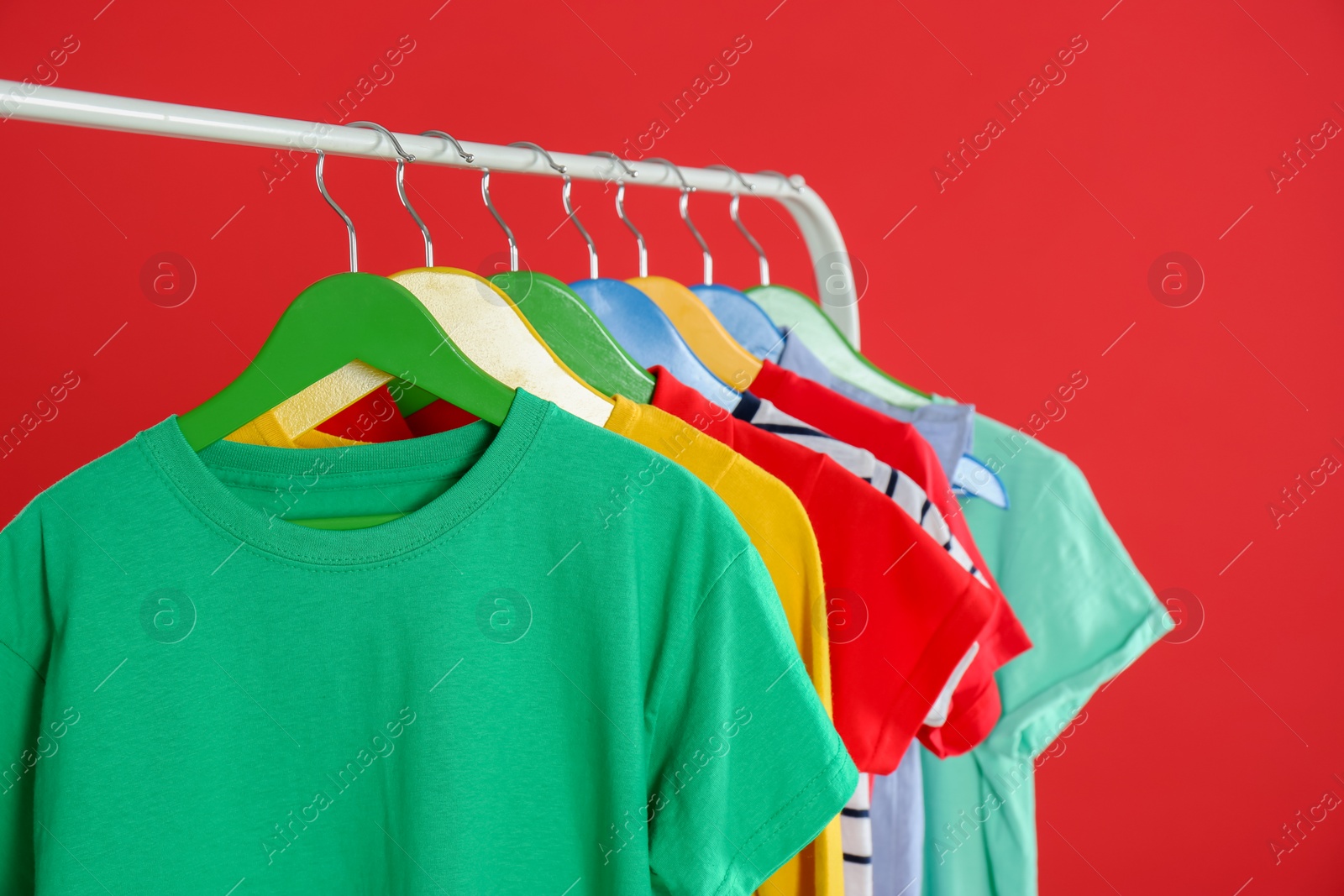 Photo of Rack with stylish children clothes on red background, closeup