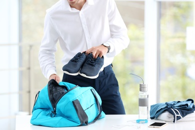 Photo of Young businessman packing sports stuff for training into bag in office