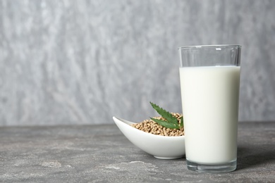 Photo of Glass of hemp milk, bowl with seeds and space for text on grey background