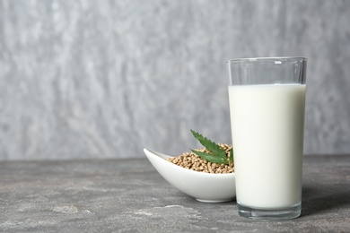 Glass of hemp milk, bowl with seeds and space for text on grey background