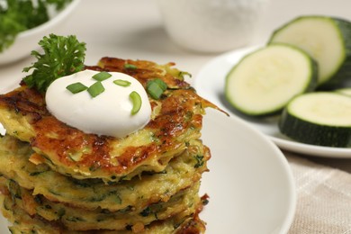 Photo of Delicious zucchini fritters with sour cream on plate, closeup. Space for text