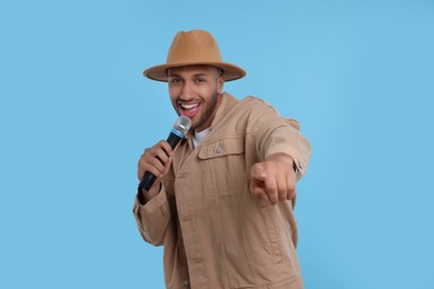 Handsome man with microphone singing on light blue background