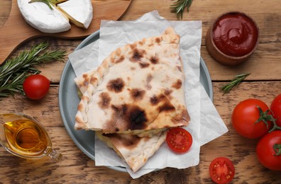 Photo of Tasty pizza calzones with cheese and different products on wooden table, flat lay
