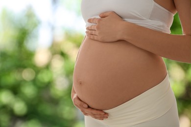 Young pregnant woman touching her belly outdoors, closeup. Space for text