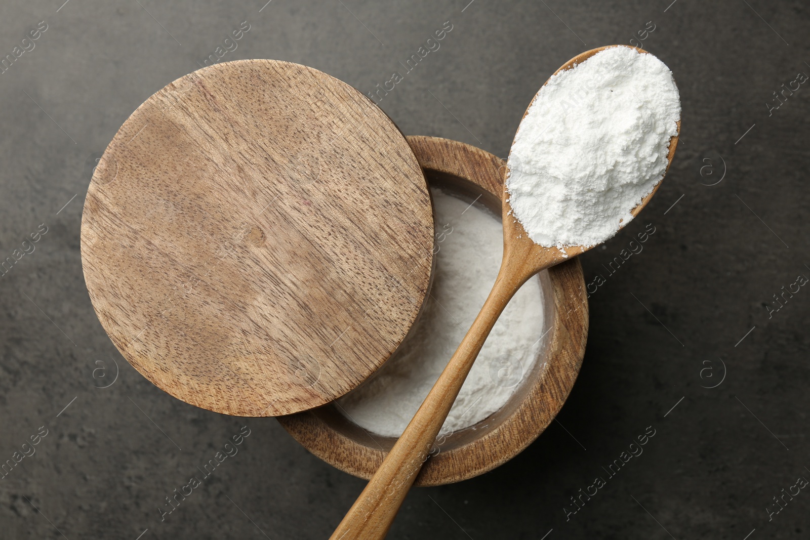 Photo of Baking powder in bowl and spoon on grey textured table, top view