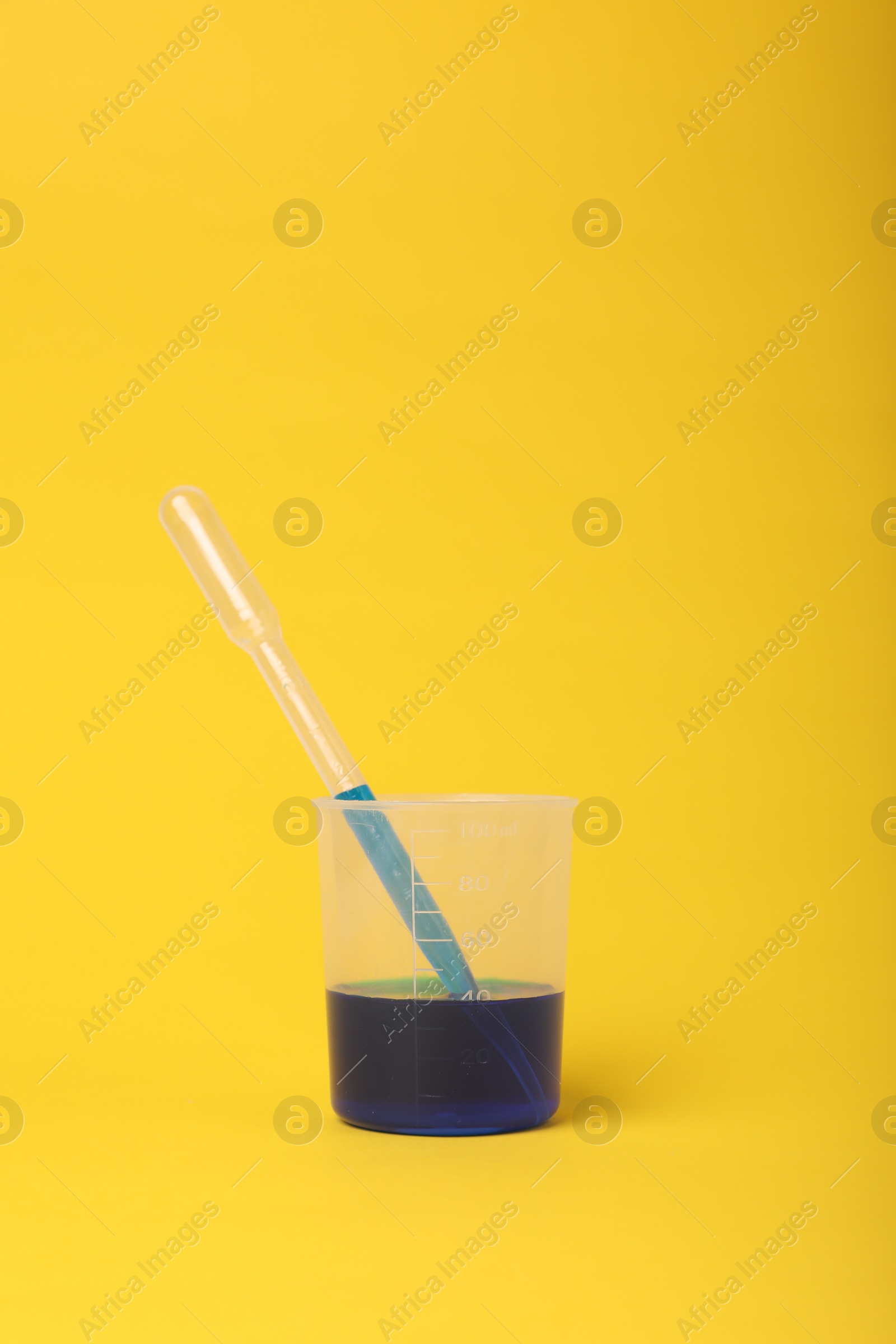 Photo of Beaker with liquid and stirring rod on yellow background. Chemical experiment toy for kids