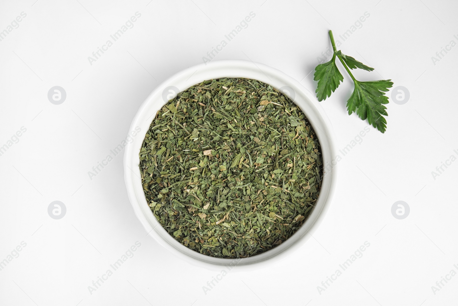 Photo of Bowl with dried parsley and fresh twig on white background, top view