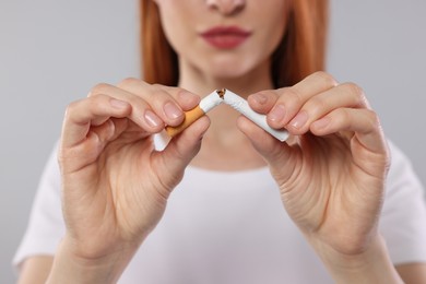 Photo of Stop smoking concept. Woman breaking cigarette on light gray background, closeup