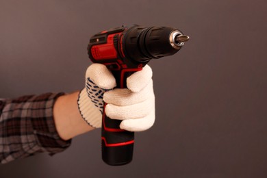 Handyman holding electric screwdriver on brown background, closeup
