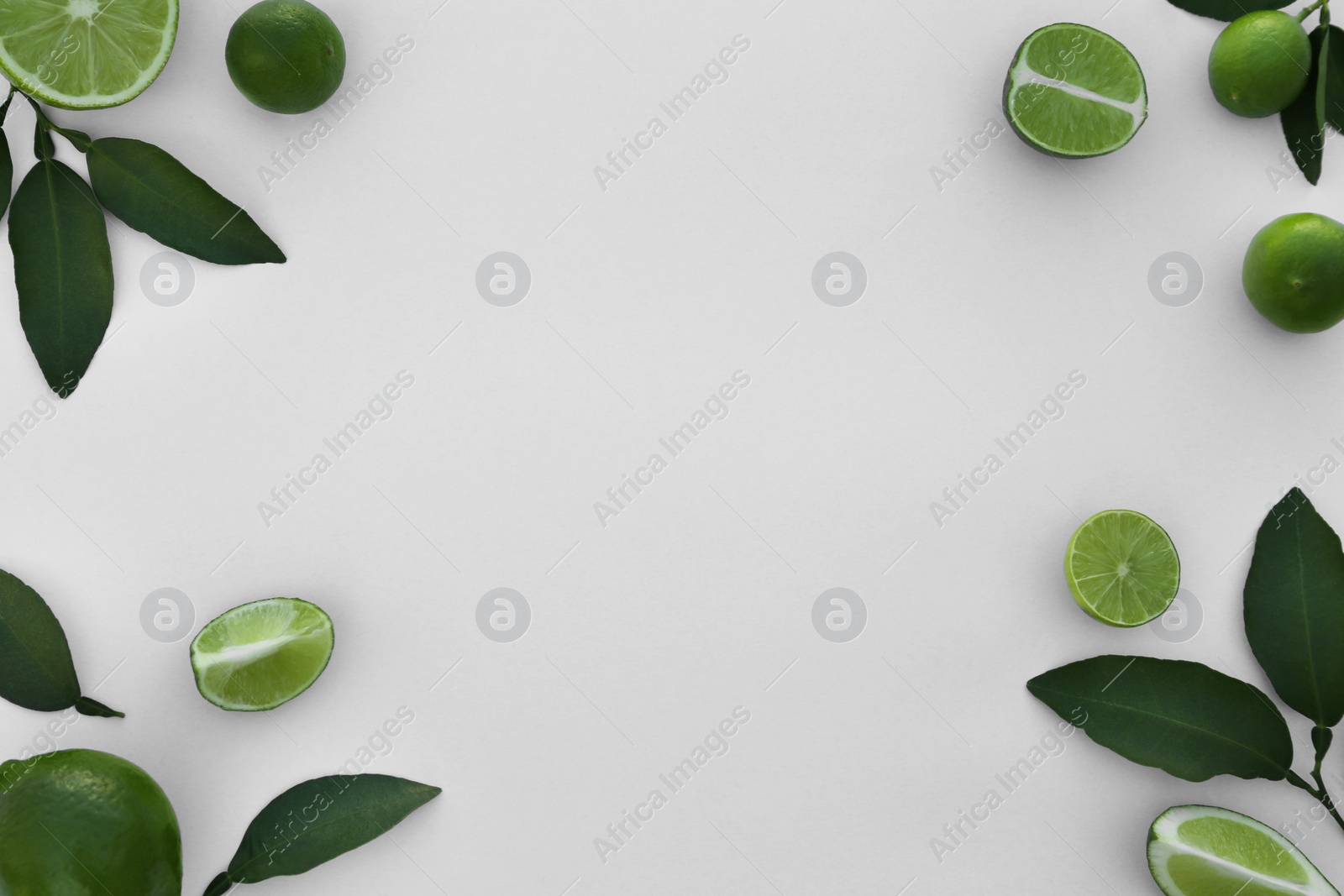 Photo of Whole and cut fresh limes with leaves on white background, flat lay. Space for text