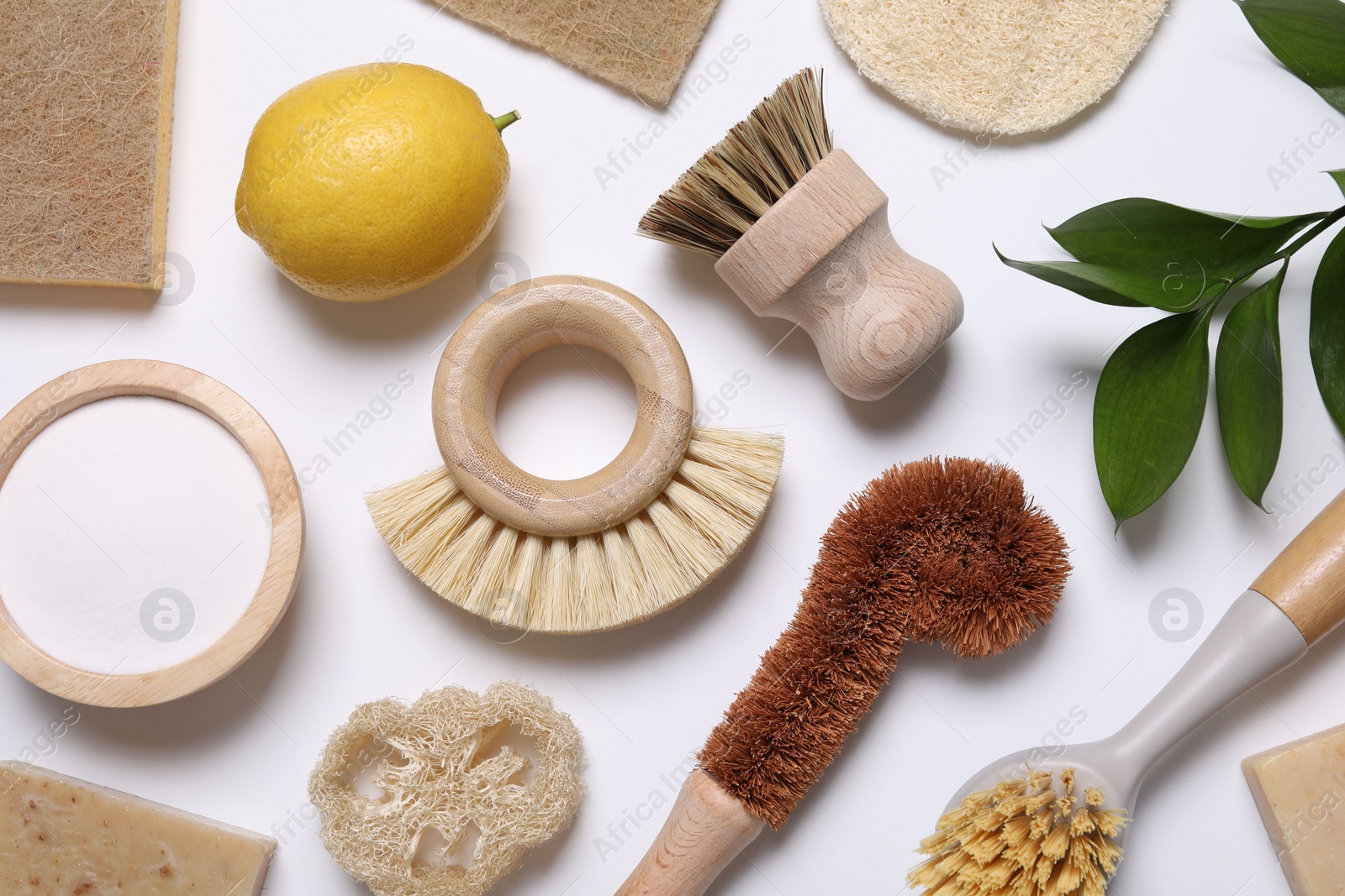 Photo of Cleaning brushes, lemon, baking soda, sponges and floral decor on white background, flat lay