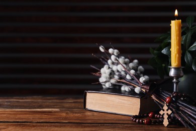 Rosary beads, Bible, burning candle and willow branches on wooden table, space for text