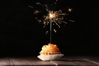Photo of Delicious dessert with burning sparkler on wooden table against dark background