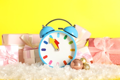Photo of Alarm clock with Christmas decor on yellow background. New Year countdown