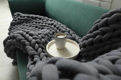 Photo of Tray with cup of coffee and soft chunky knit blanket on sofa indoors