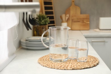 Jug and glasses with clear water on white table in kitchen, space for text