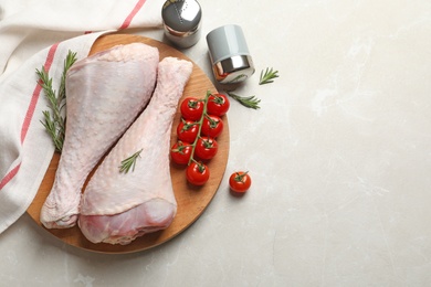 Photo of Board with raw turkey drumsticks, tomatoes and rosemary on light background, flat lay. Space for text