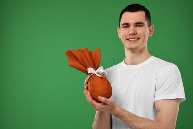 Photo of Easter celebration. Handsome young man with wrapped gift on green background. Space for text