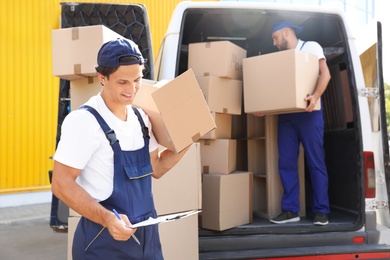 Photo of Male mover with box and clipboard near van outdoors