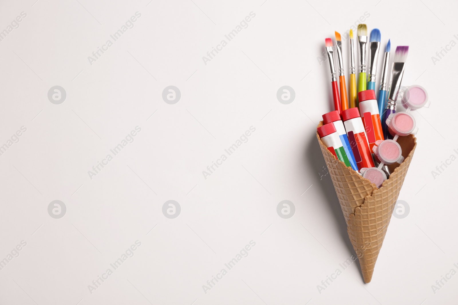 Photo of Waffle cone with different paints and brushes on white background, top view. Space for text