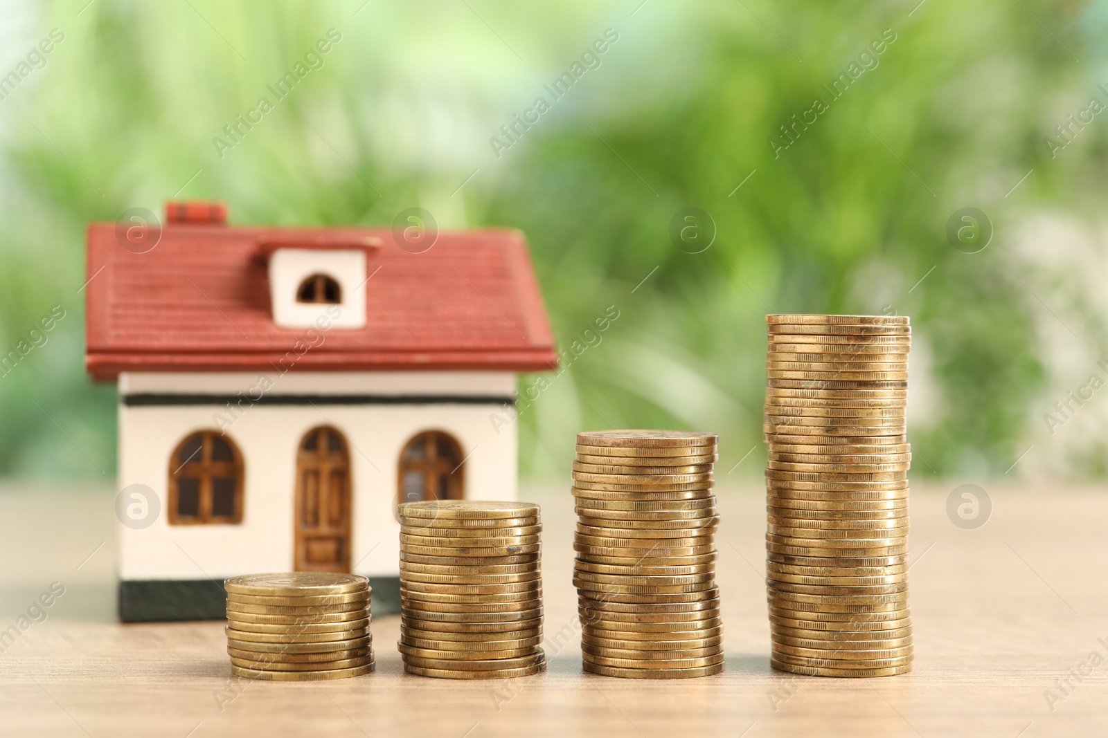 Photo of Mortgage concept. Model house and stacks of coins on wooden table against blurred green background, closeup