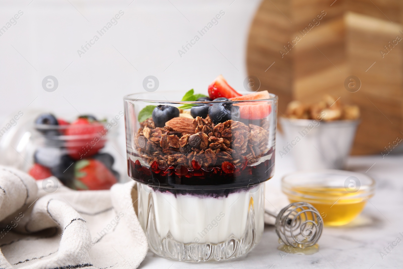 Photo of Tasty granola with berries, jam and yogurt in glass on white table