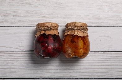 Jars with pickled fruits on white wooden table, flat lay