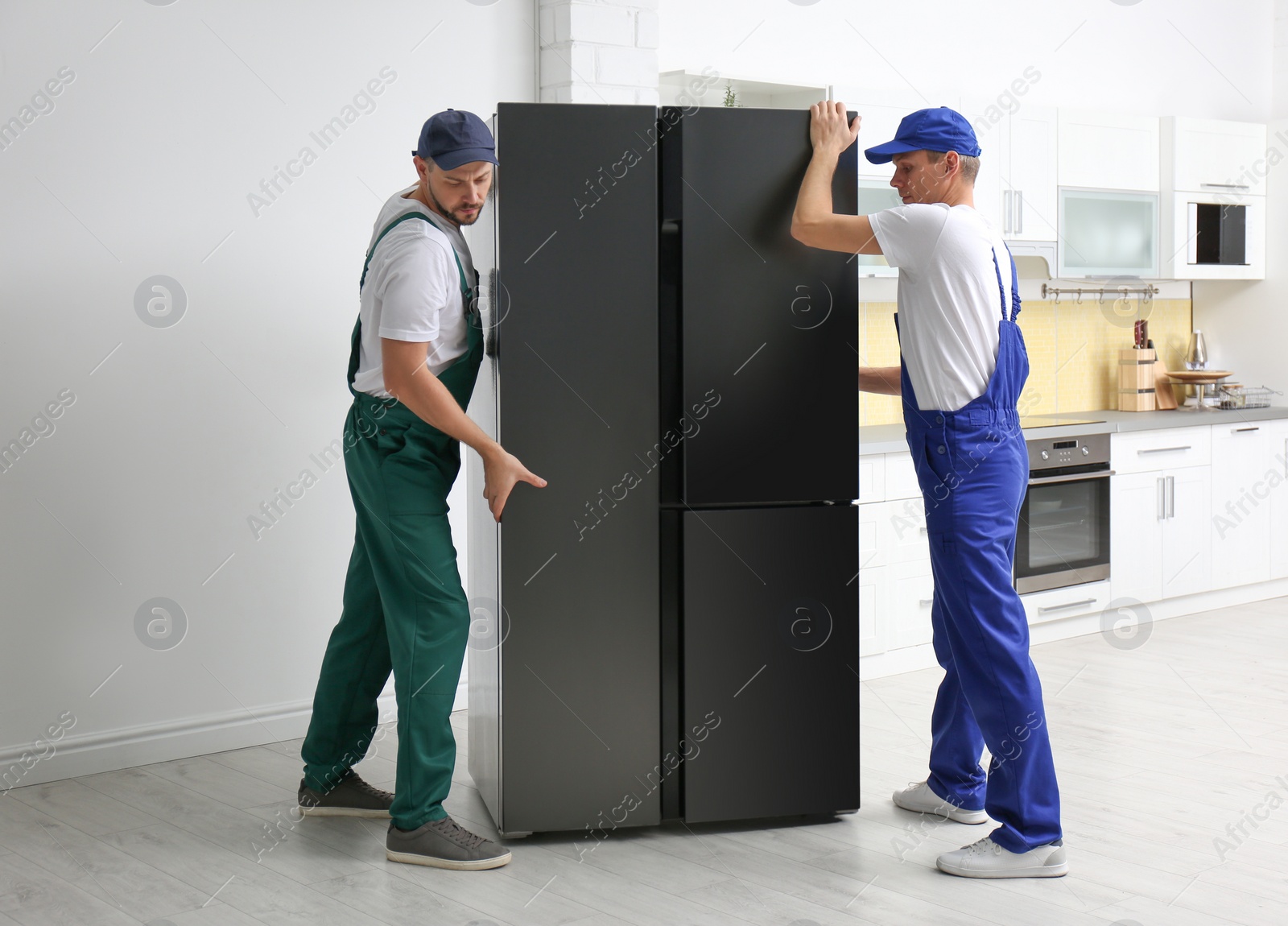 Photo of Professional workers carrying modern refrigerator in kitchen