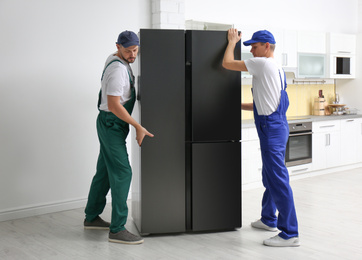 Professional workers carrying modern refrigerator in kitchen