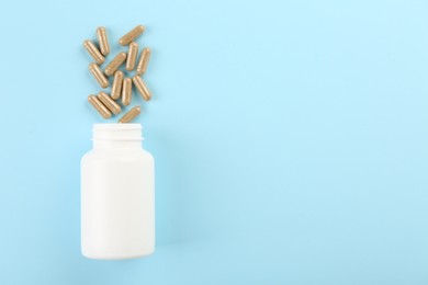 Photo of Bottle and vitamin capsules on light blue background, top view. Space for text