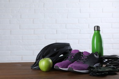 Different cycling accessories on wooden table against white brick wall, space for text