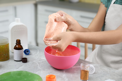 Little girl kneading DIY slime toy at table indoors, closeup