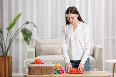 Young woman rolling shirt at table in room, space for text. Organizing clothes