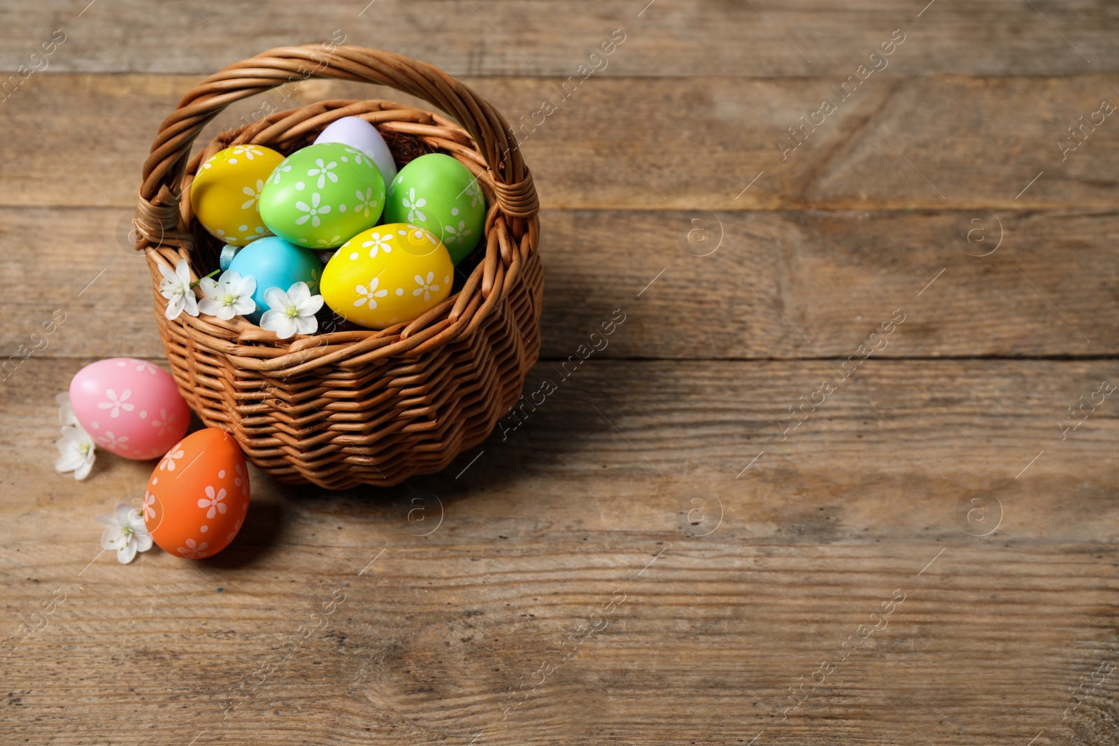 Photo of Colorful Easter eggs in basket and flowers on wooden background. Space for text