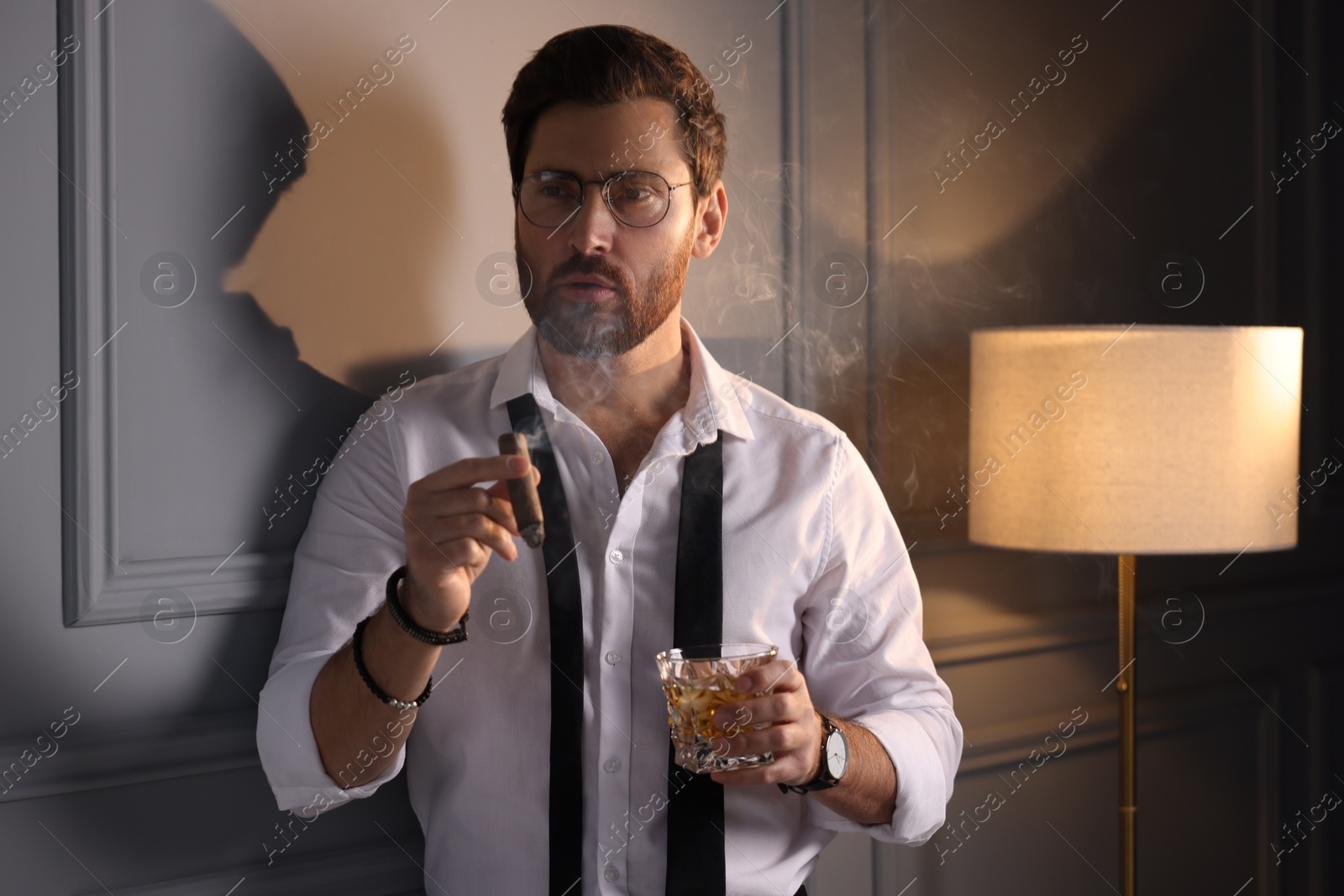 Photo of Handsome man with glass of whiskey smoking cigar at home