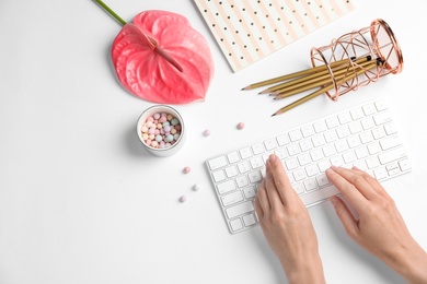 Woman using computer keyboard on white table decorated with tropical flower, top view. Creative design ideas